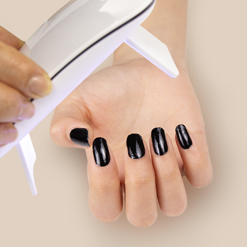 Hand with black nail wraps curing with a UV/LED lamp.