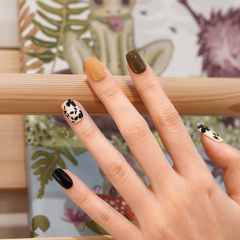 Hand wearing a mix of earthy autumn shades and bold black florals nail wraps.