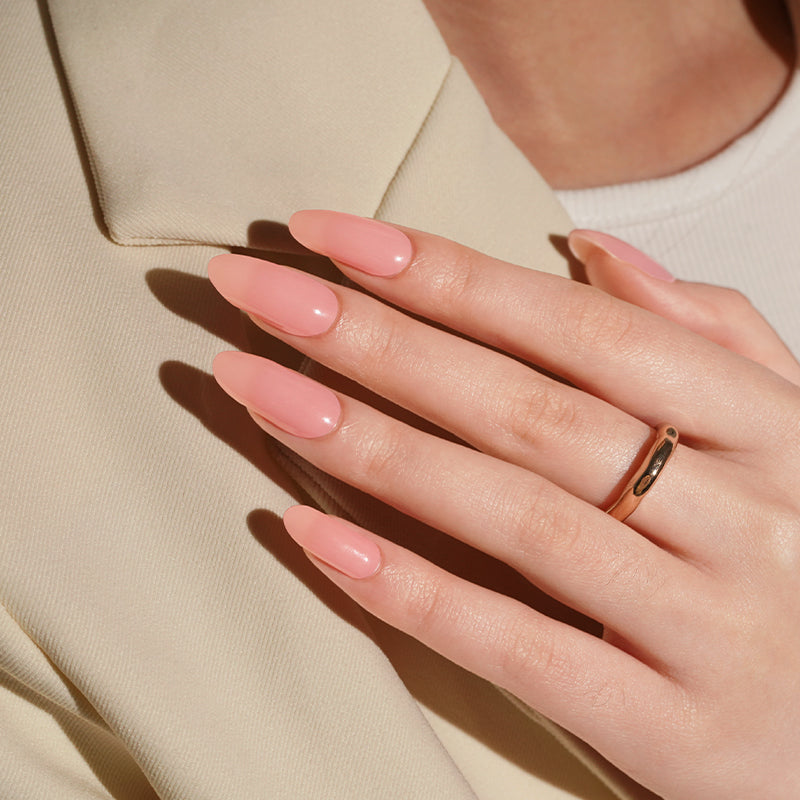 Close-up of a hand with pink nail polish wraps wearing a gold ring on a beige background