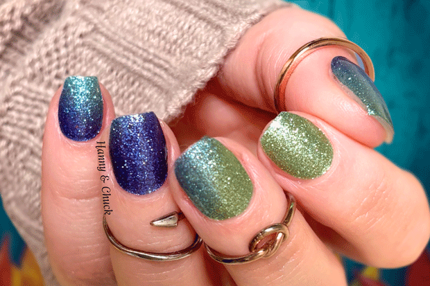 Hand with glittery blue and green nail wraps wearing multiple rings against a blurred background