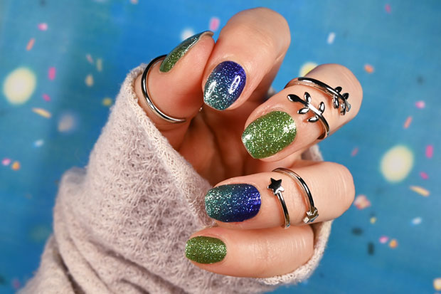 A person's hand showcasing nail wraps with a mix of bright blue and green glitters.