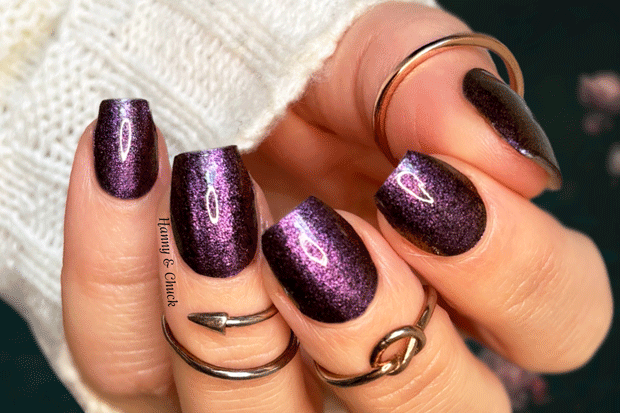 Hand with purple glittery nails and multiple rings on a blurred background