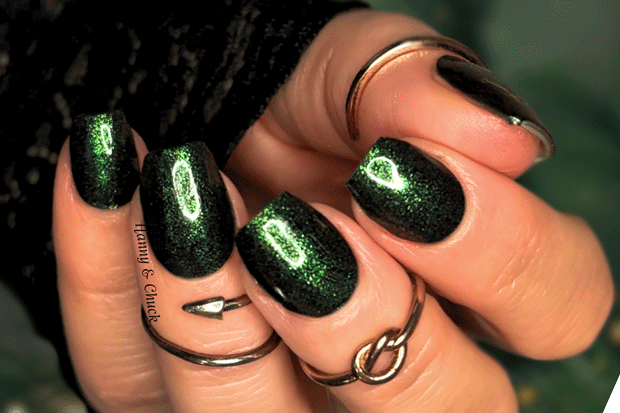Hand with green glittery nail polish wraps wearing multiple rings on a blurred background