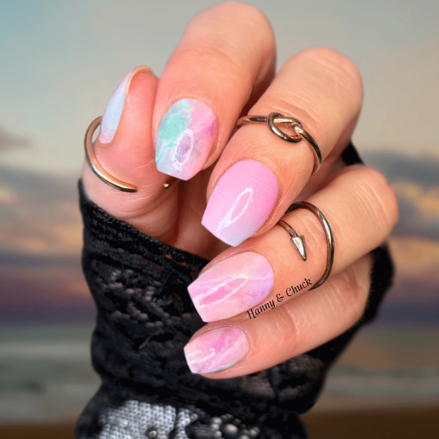 Hand with pink and white nail polish stickers against a blurred beach sunset background