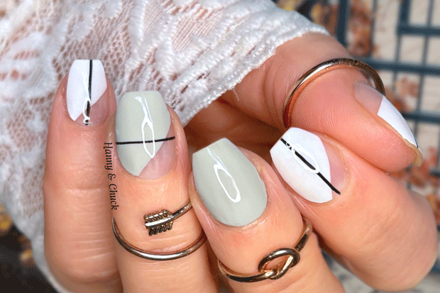 Close-up of a hand with light gray and white nail polish strips, wearing rings.