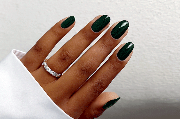 Hand with dark green nail polish wraps wearing a silver ring on a white background