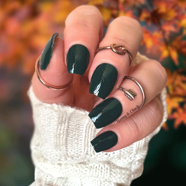 Hand with dark green nail polish wraps against a blurred autumn leaf background