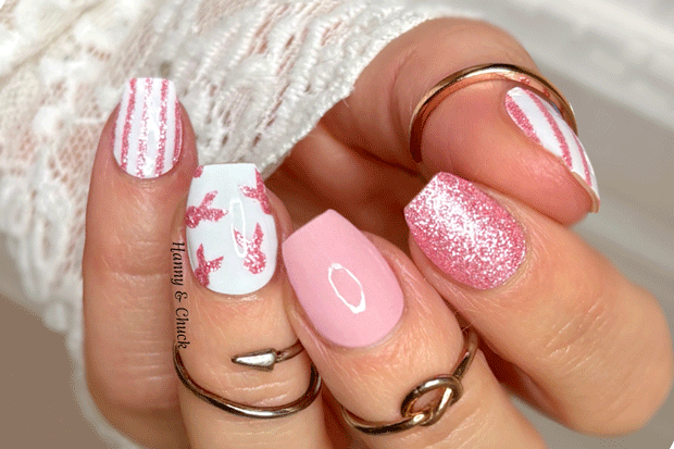 Close-up of a hand with pink and white nail polish wraps, wearing multiple rings on a pink background.