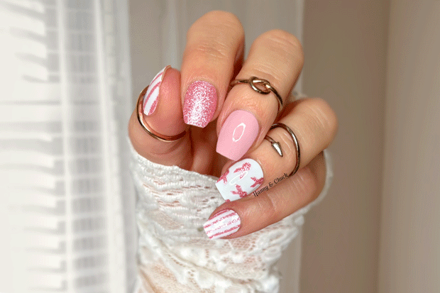 Close-up of a hand with pink and white nail polish wraps, wearing multiple rings on a pink background.