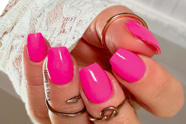 Close-up of a hand with bright pink nail polish wraps wearing gold rings.