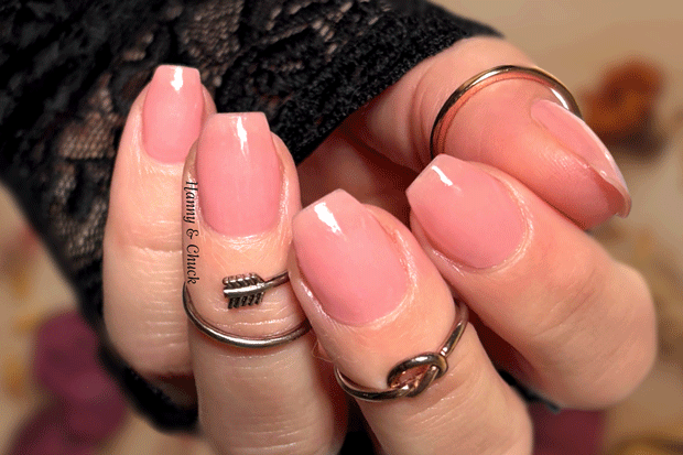 Close-up of a hand with pink nail polish wraps and multiple rings on a blurred background