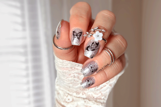 Hand with decorative silver glitter nail wraps  and rings on a blurred background
