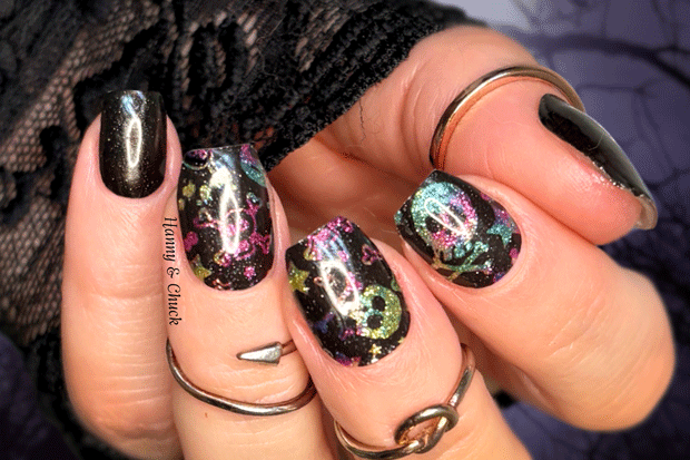 Close-up of a hand with black and multicolored glitter halloween nail wraps, wearing multiple rings.