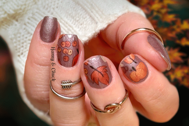 Nails with autumn-themed nail wrap design and rings on a blurred background