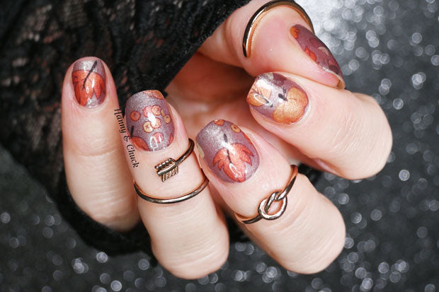 Nails with autumn-themed nail wrap design and rings on a blurred background