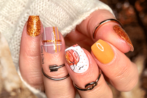 Close-up of a hand with intricately designed nail wraps featuring gold, mauve, and orange colors.