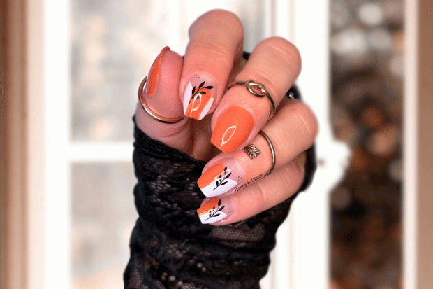 Hand with orange and white nail wrap art, blurred autumn background