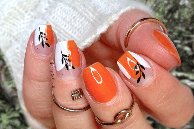 Close-up of a hand with orange and white nail polish wraps on a blurred natural background