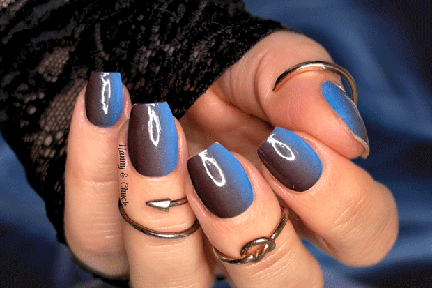 Hand with blue and black gradient nails wearing multiple rings on a dark background