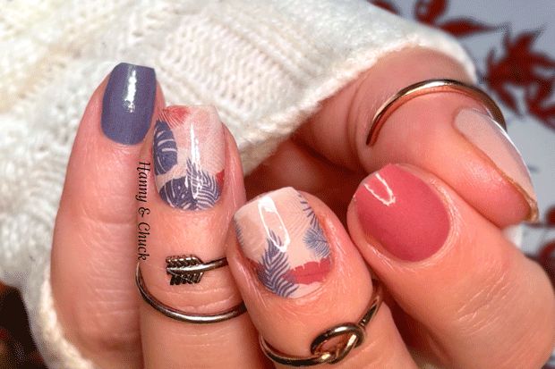 Close-up of a hand with blue and coral nail wraps with a tropical leaf pattern against a blurred background