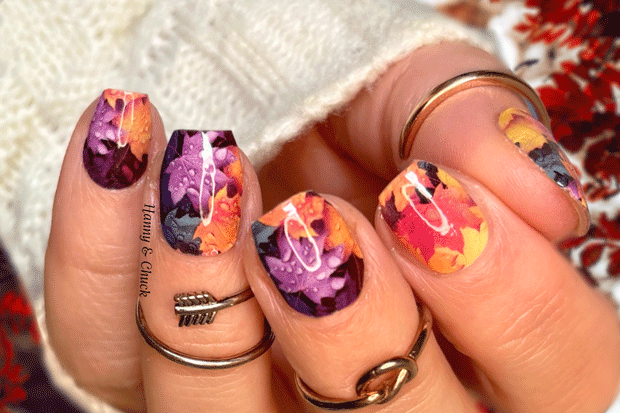 Nails with colorful Canadian maple leaf designed nail wraps on a person wearing rings.